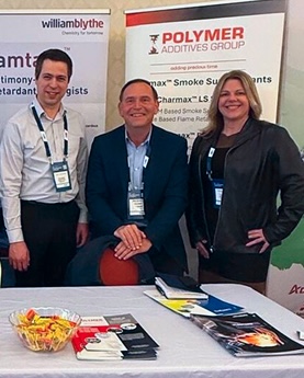Polymeradditivesgroup | Polymer Additives Group Pag Employees Stand Together by Their Table at a Convention.